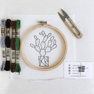 Cactus embroidery kit with thread, hoop, thread snips, and needle taped to a business card.