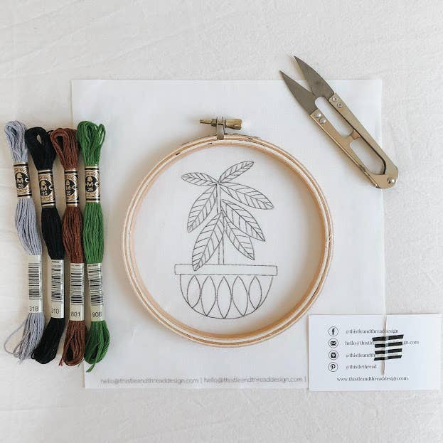 Image of an embroidery kit showing thread, hoop, fabric, thread snips, and a needle taped to a business card